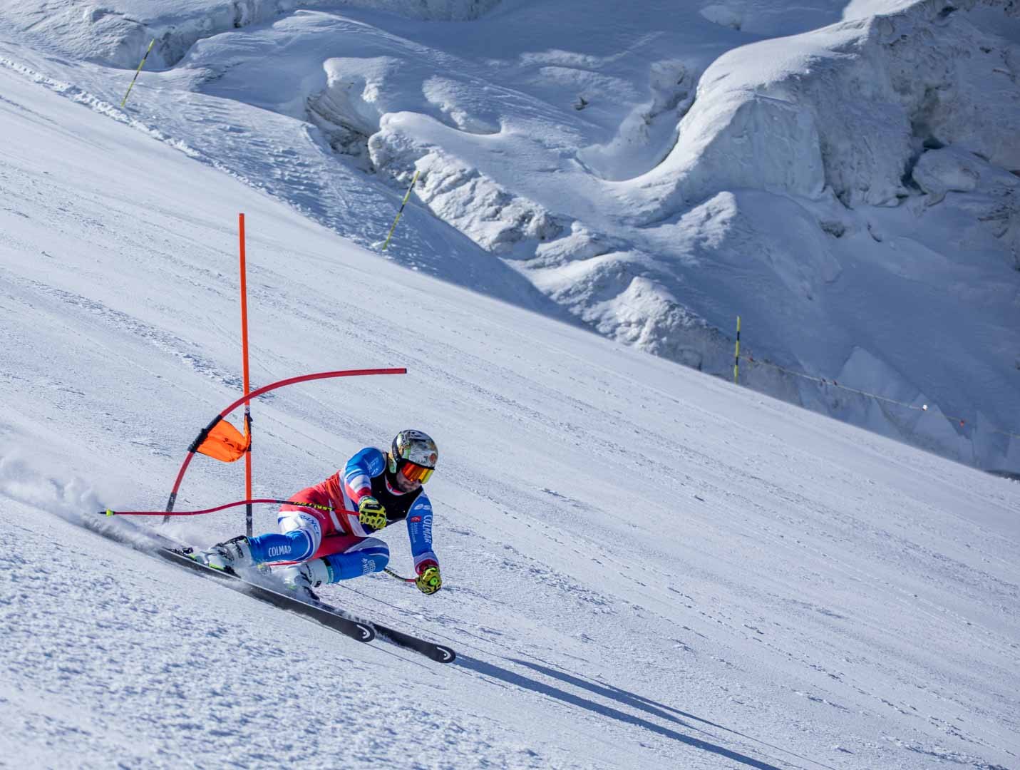 Alpine skier carving through a giant slalom course above a glacier