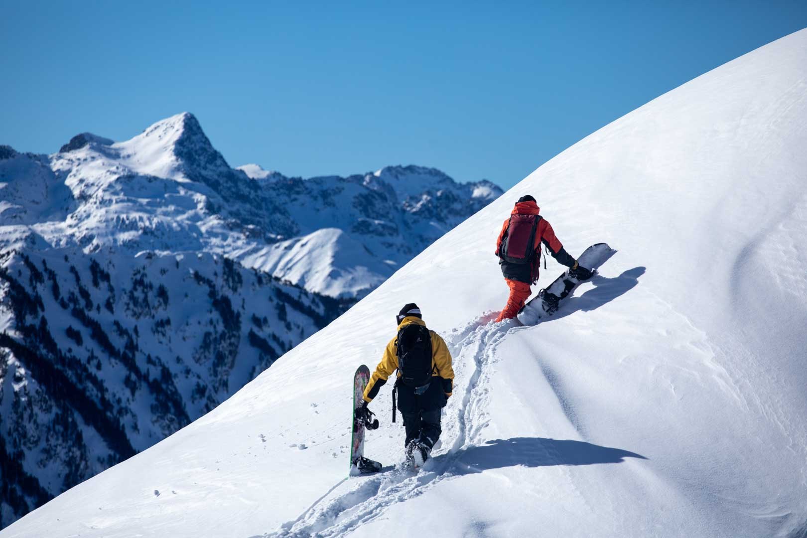 Snowboarders climbing a bright mountain ridge