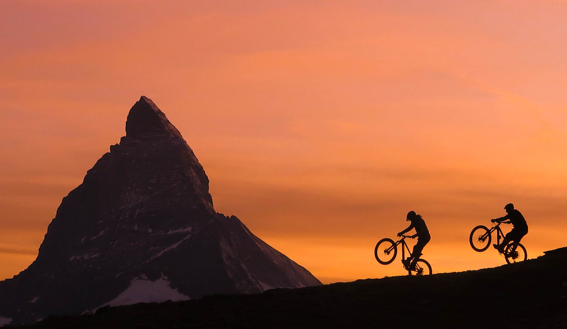 Enduro riders silhouetted against a vivid sunset