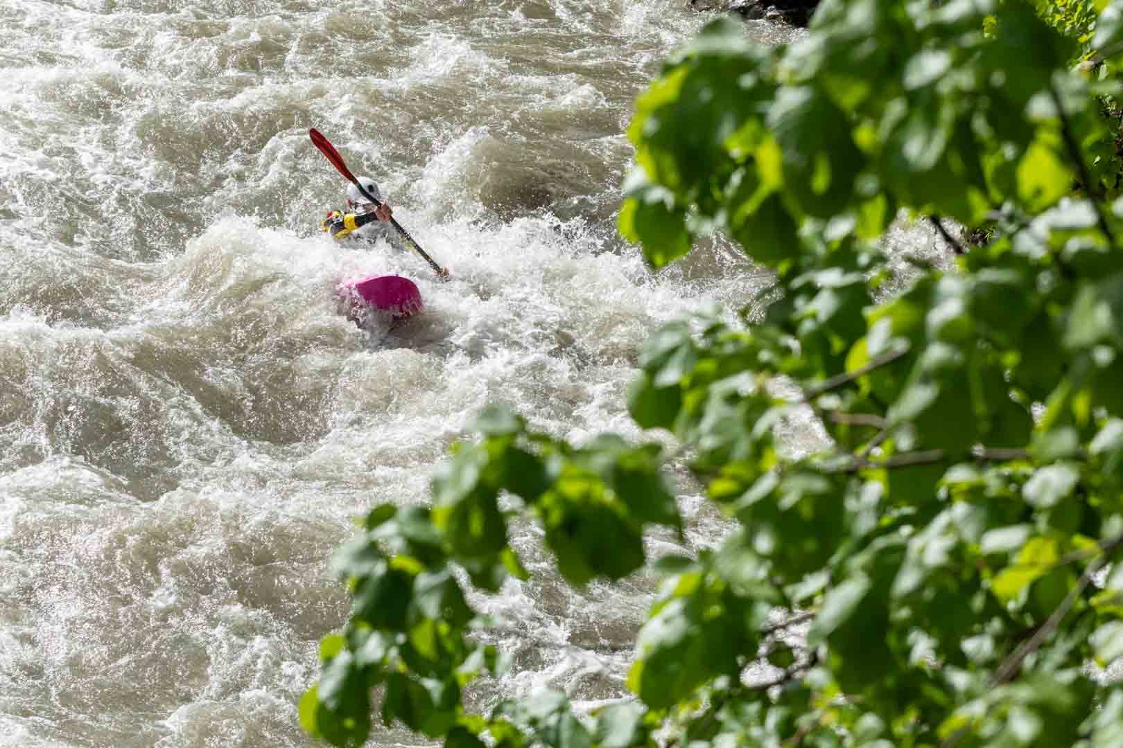 Kayaker navigating wild water behind green leaves