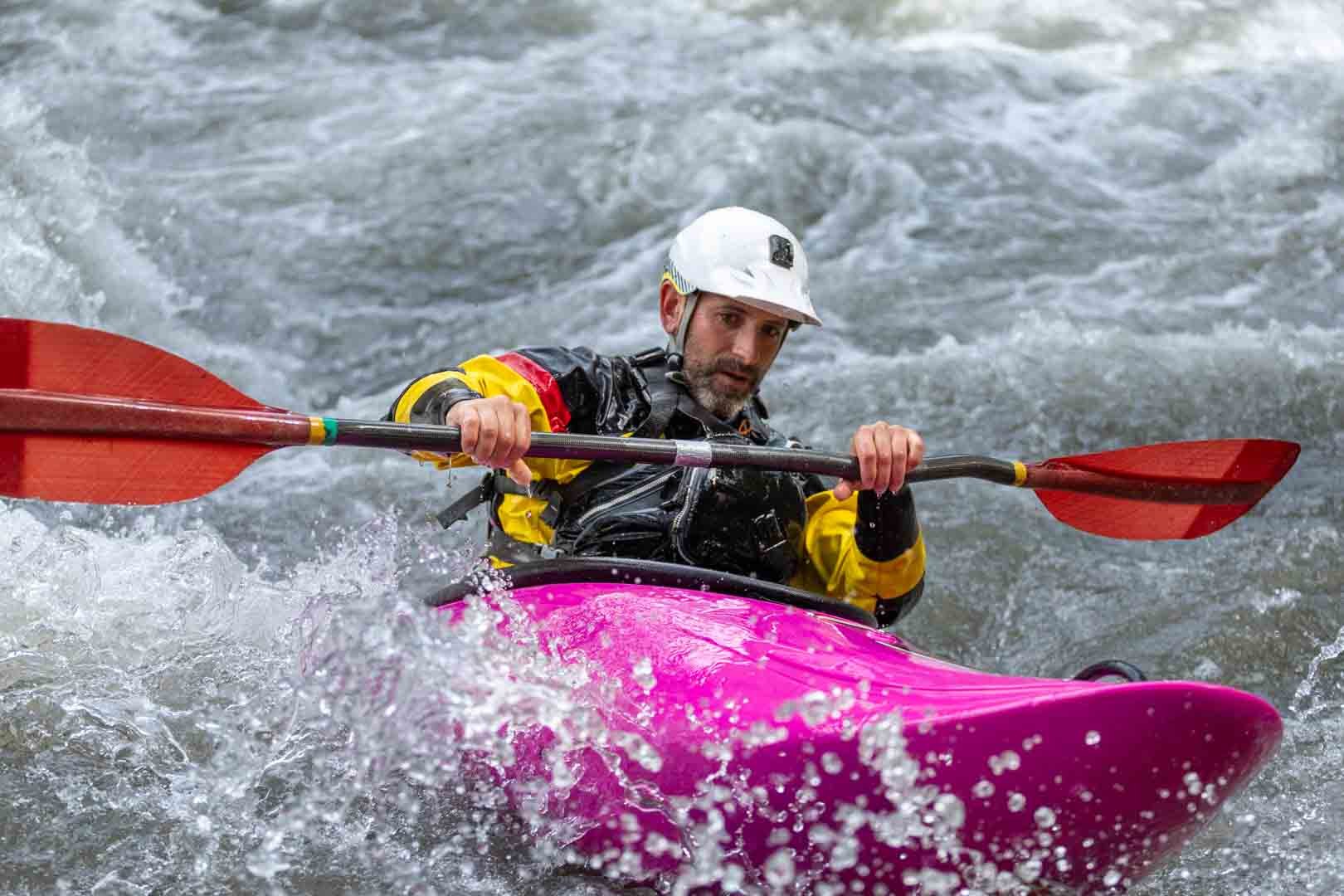 Kayaker cutting through wild water in a magenta kayak