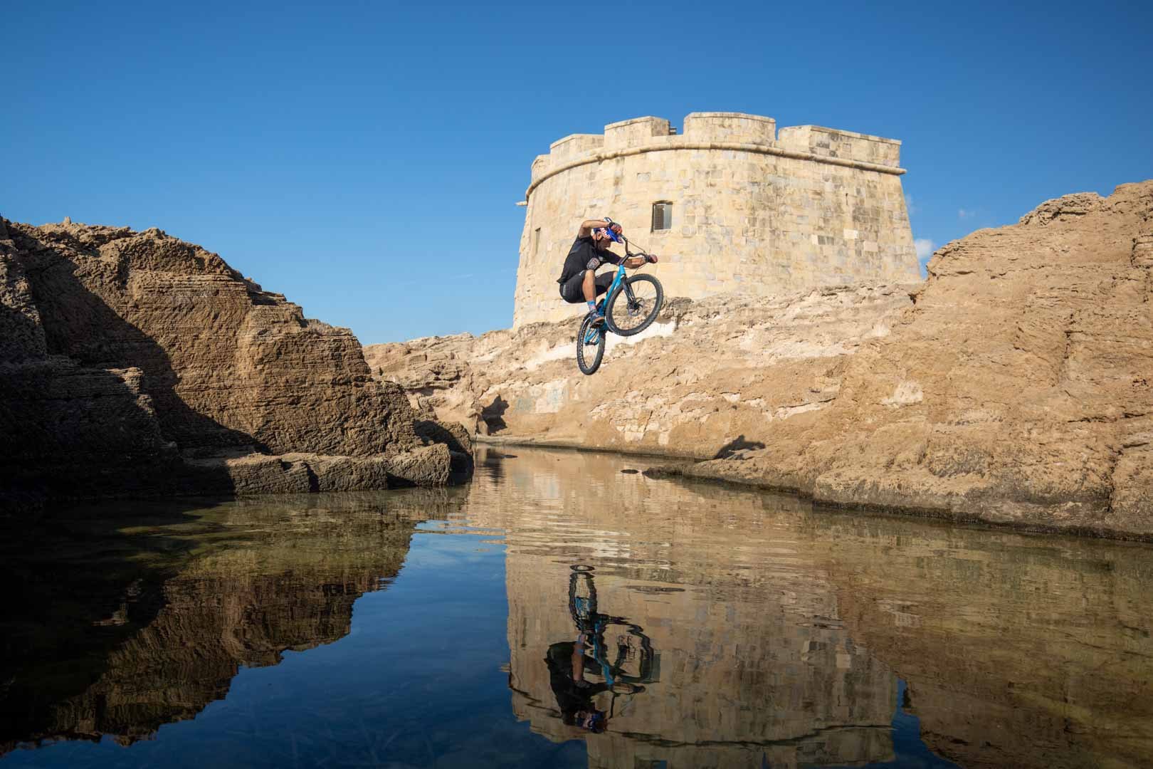 Bike trials rider jumping above a reflective rock pool