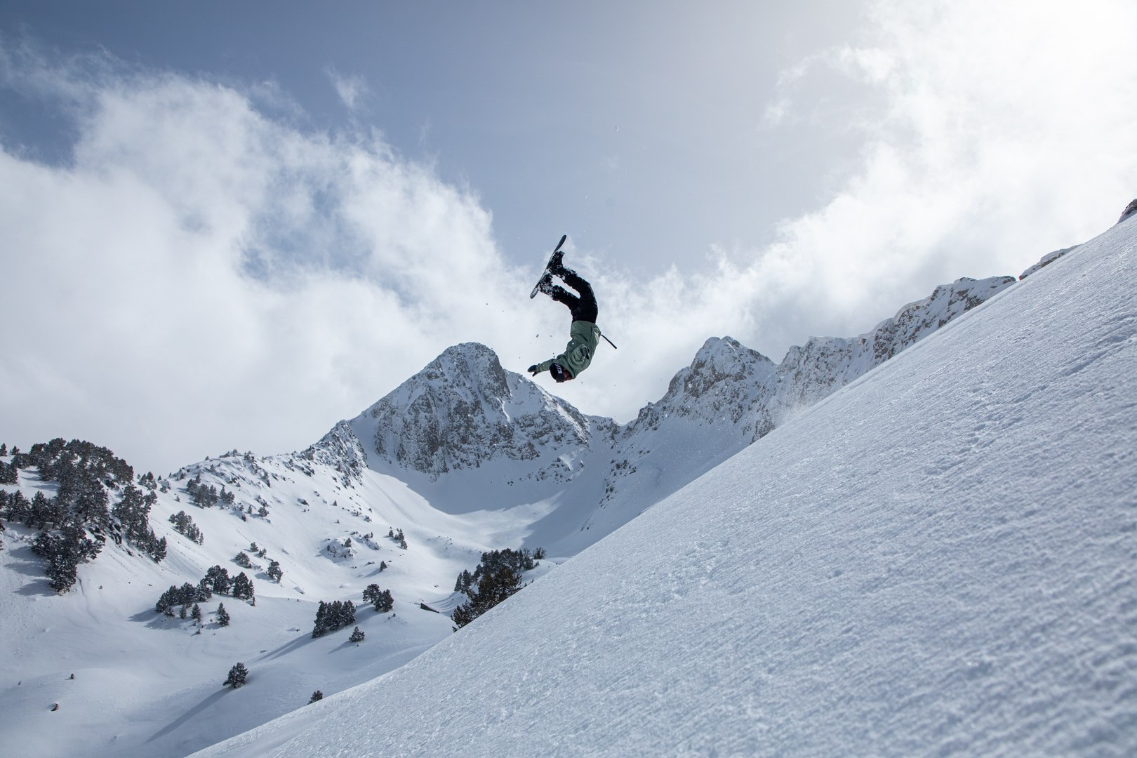 Snowboarder rotating above a snowy mountain bowl
